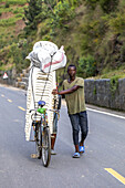 Mann schiebt eine Ladung Plastikstühle auf einem Fahrrad im Westen Ruandas, Afrika