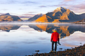 Ein Fotograf beobachtet Berge und Rorbuer in einem Fjord bei Sonnenuntergang, Leknes, Vestvagoy, Nordland, Lofoten, Norwegen, Skandinavien, Europa