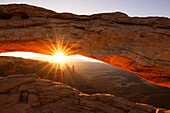 Sonnenlicht umhüllt das Canyonlands Valley während eines Sonnenaufgangs im Sommer, eingerahmt vom Mesa Arch, Utah, Vereinigte Staaten von Amerika, Nordamerika