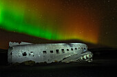 Ein abgestürztes DC-3-Flugzeug unter den Polarlichtern (Aurora Borealis) in Island, Polargebiete