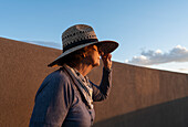 USA, New Mexico, Santa Fe, Frau mit Strohhut an einer Lehmziegelwand in der Hochwüste
