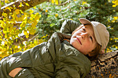 USA, New Mexico, Nachdenklicher Junge, der auf einem Baumstamm im Santa Fe National Forest liegt