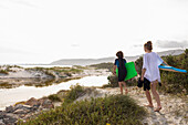 Südafrika, Hermanus, Bruder und Schwester gehen mit Bodyboards am Strand spazieren