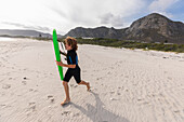 Südafrika, Hermanus, Lächelnder Junge, der mit einem Bodyboard am Strand läuft