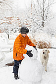 Junge mit seinem Hund baut Schneemann