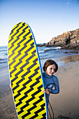 Mexico, Baja, Pescadero, Boy carrying surfboard on beach