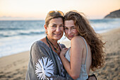 Porträt einer lächelnden Mutter und ihrer Tochter im Teenageralter am Strand