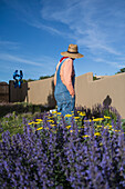 USA, New Mexico, Santa Fe, Frau mit Strohhut und Jeans-Overall steht im Garten