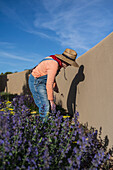 USA, New Mexico, Santa Fe, Frau mit Strohhut und Jeans-Overall bei der Gartenarbeit