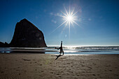 USA, Oregon, Silhouette of woman doing cartwheel near Haystack Rock at Cannon Beach