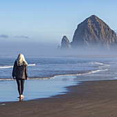 USA, Oregon, Rückansicht einer Frau bei einem Spaziergang in der Nähe des Haystack Rock in Cannon Beach im Morgennebel