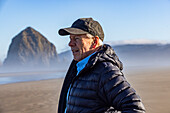 USA, Oregon, Man standing near Haystack Rock at Cannon Beach in morning mist