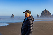 USA, Oregon, Man standing near Haystack Rock at Cannon Beach in morning mist