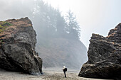 USA, Oregon, Brookings, Ältere Frau steht zwischen Felsen am Strand