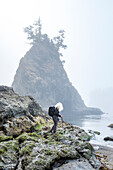 USA, Oregon, Brookings, Ältere Frau wandert auf Felsen über dem Meer