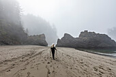 USA, Oregon, Brookings, Senior woman hiking with nordic walking poles on beach