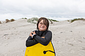 Lächelnder Junge (10-11) hält Bodyboard am Strand