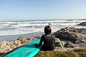 South Africa, Hermanus, Boy (10-11) with surfboard sitting on Kammabaai Beach