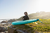 Boy (10-11) with surfboard sitting on Kammabaai Beach
