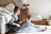 Teenage girl (16-17) playing guitar in bedroom