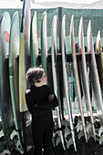 Junge (10-11) posiert vor einem Surfbrett
