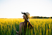 Rear view of woman in straw hat standing in field at sunset