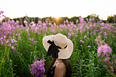 Side view of young woman looking at flowers on meadow