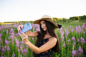 Junge Frau macht Selfie auf der Wiese stehend