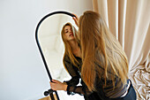 Junge Frau schaut in den Spiegel in einer Wohnung