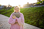Frau umarmt Laptop, während sie bei Sonnenaufgang im Freien steht