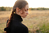 Side view of serious woman standing in field at sunset