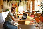 Seitenansicht einer Frau, die sitzend im Café am Laptop arbeitet