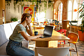 Side view of woman working on laptop while sitting in cafe 