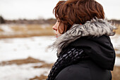 Porträt einer nachdenklichen Frau mit Blick auf ein Feld in einer Winterlandschaft