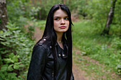Porträt einer nachdenklichen Frau in Lederjacke, die im Wald steht