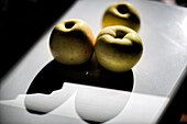 Drei Äpfel werfen Schatten auf eine spiegelnde Oberfläche