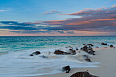 Langzeitbelichtung der Brandung des Indischen Ozeans, die bei Sonnenuntergang auf einen felsigen Strand trifft. Anse Bambous Strand, Fregate Insel, Seychellen.