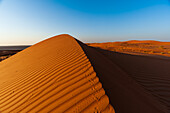 Fußabdrücke entlang des Kammes einer Sanddüne bei Sonnenuntergang. Wahiba Sands, Arabische Halbinsel, Oman.