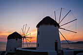 Windmühlen im traditionellen Stil an der Küste bei Sonnenuntergang. Chora, Insel Mykonos, Kykladeninseln, Griechenland.