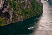 Ein Kreuzfahrtschiff fährt an steilen Klippen im Geirangerfjord, Norwegen, vorbei.