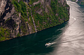 A cruise ship navigates past sheer cliffs in Geirangerfjord, Norway.