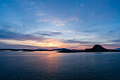 Die Sonne geht hinter silhouettierten Inseln in der Norwegischen See bei Bronnoysund unter. Norwegisches Meer bei Bronnoysund, Bronnoy, Norwegen.