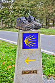 Spanien, Galicien. Entfernungsmarkierung auf dem Jakobsweg mit einem Paar abgetragener Schuhe. (Nur für redaktionelle Zwecke)