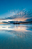 Der Huntington Beach Pier und Spiegelungen auf dem nassen Strand bei Sonnenuntergang. Huntington Beach, Kalifornien.