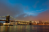 Manhattan skyline and the Brooklyn bridge in the mist at dusk.