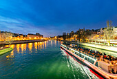 A boat tour glides on the Seine past Île de la Cité during evening twilight.