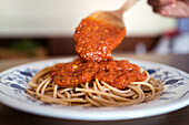 Closeup of unrecognizable cook garnishing tasty spaghetti with marinara sauce prepared for lunch