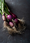 From above of fresh ripe purple onions with green stems placed on black table