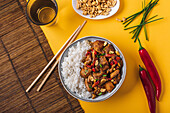 Kompositionsschüssel mit Kung-Pao-Hühnchen mit weißem Reis, Erdnuss, roter Chilischote, grüner Zwiebel und Stäbchen von oben