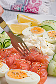 Closeup of anonymous person with fork eating tasty smoked salmon served on plate with boiled eggs and cream cheese